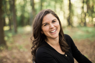 Smiling woman named Holly Tomlinson stands in a forest with trees in the background.